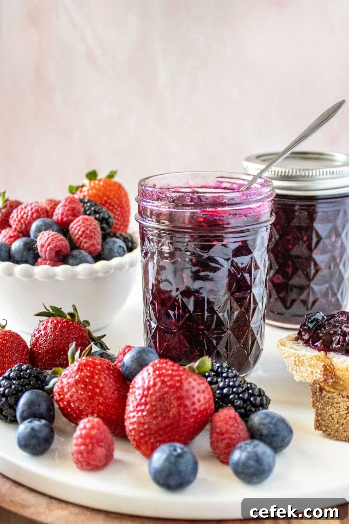 Jar of Mixed Berry Jam with a spoon in it, sitting on a marble plate with some fresh berries around the edge.