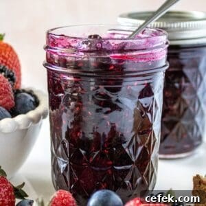 Jar of Mixed Berry Jam with a spoon in it, sitting on a marble plate with some fresh berries around the edge.