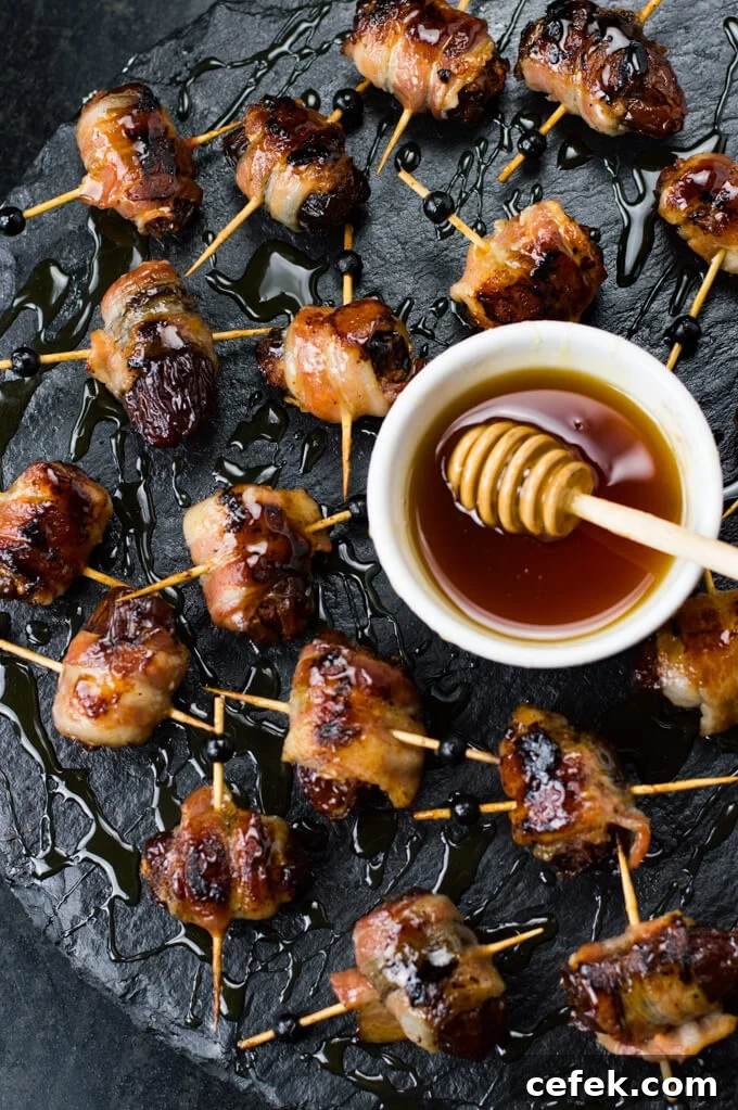 Bacon wrapped chorizo stuffed dates scattered on a black serving tray. A white bowl of honey with a honey drizzler in it.