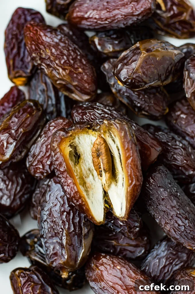 A bunch of dates with one opened and a seed in the middle of it.