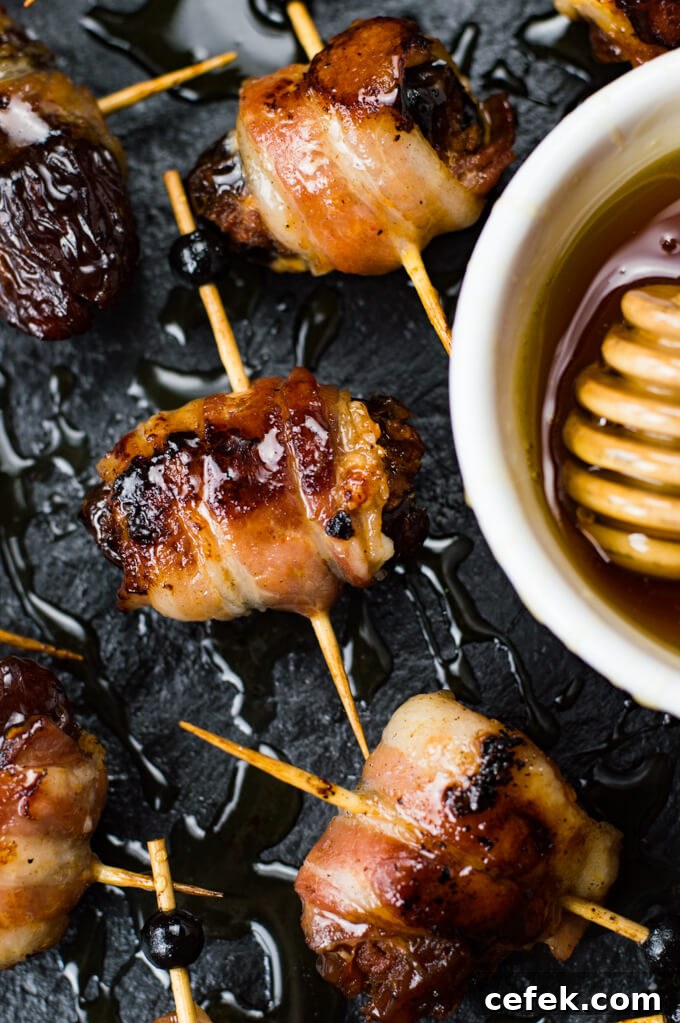 A close-up of dates that are stuffed with chorizo and wrapped in bacon. A small bowl of honey sits next to them.