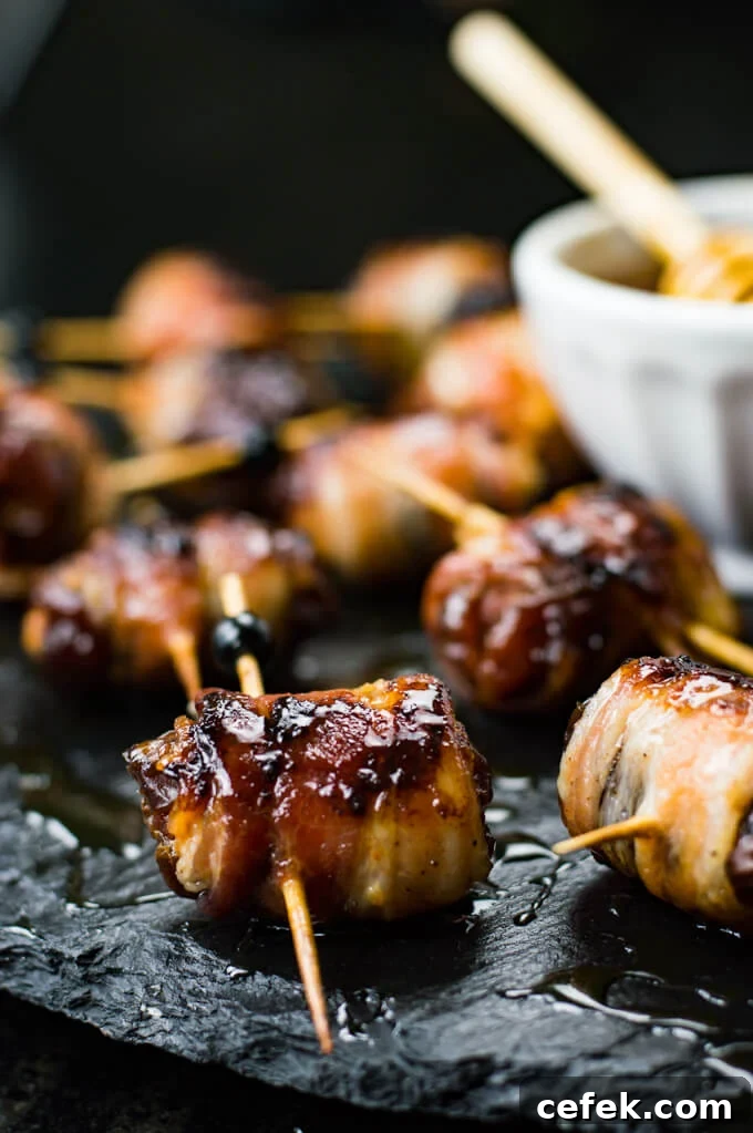 A close-up of dates that are stuffed with chorizo and wrapped in bacon. A small bowl of honey sits next to them.