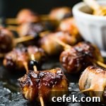 A close-up of dates that are stuffed with chorizo and wrapped in bacon. A small bowl of honey sits next to them.