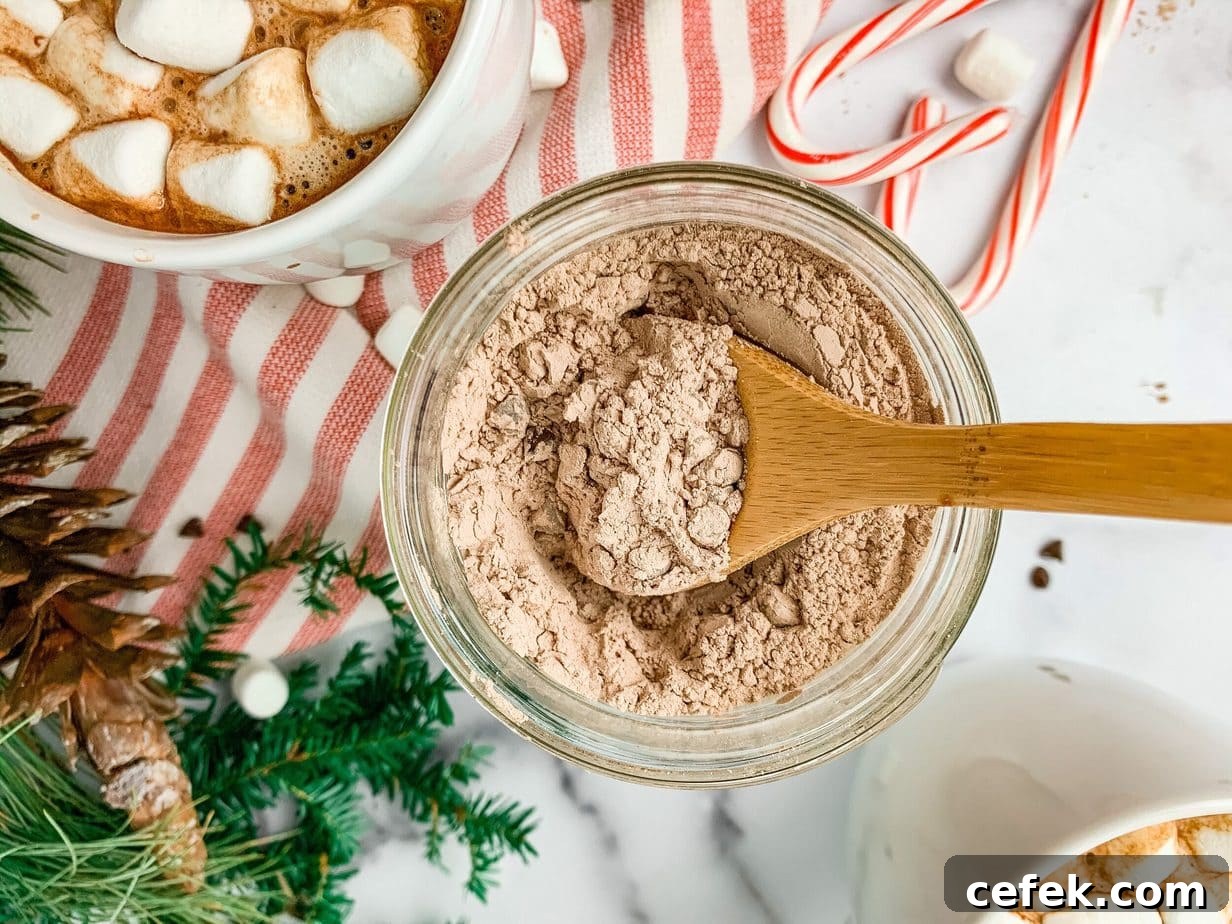 A top down view of a wooden spoon scooping out hot chocolate mix. A mug of cocoa, candy canes and greenery decor in the background.