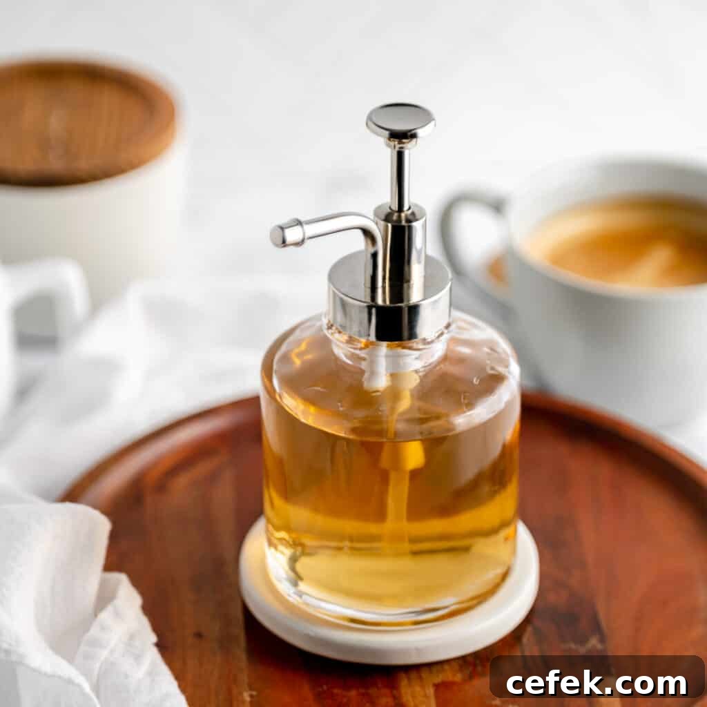 Vanilla syrup in a pump bottle with coffee and decorative dishes in the back