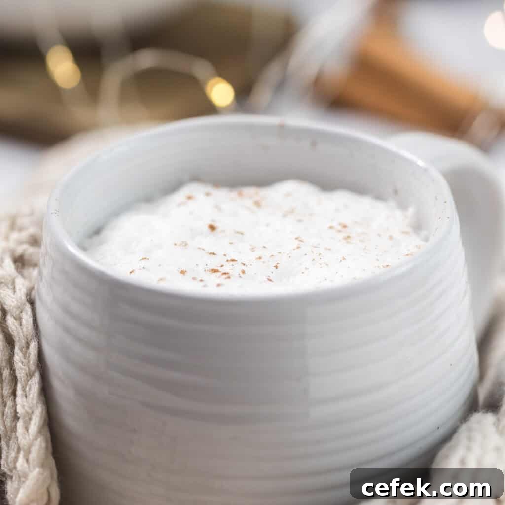 A close up of a foamy latte in a mug wrapped in a cloth. Fairy lights in the background.