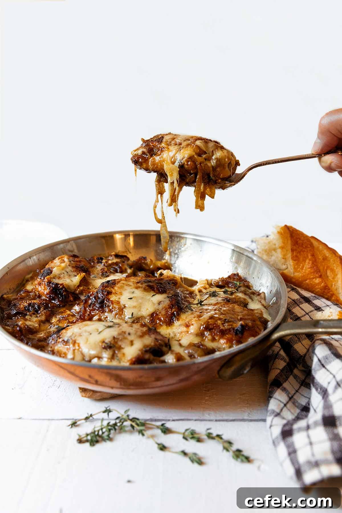 French onion skillet chicken in a copper frying pan with a person lifting out a serving