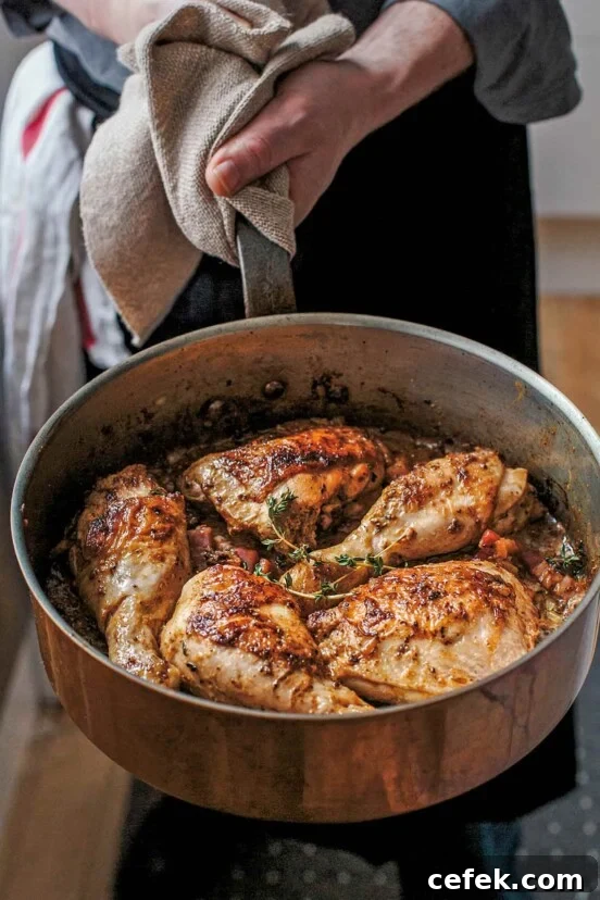 Chicken with mustard in a large metal skillet garnished with thyme, being held by a man.