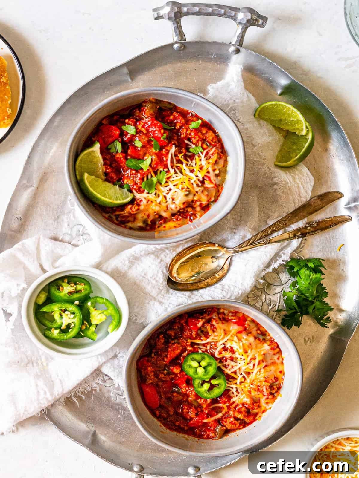 Two bowls of chili on a tray with cilantro and jalapeño slices.