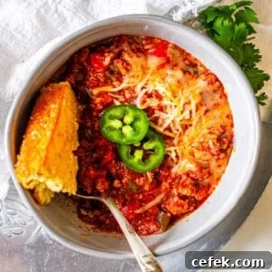 A bowl of chili topped with jalapeno slices and a piece of cornbread.