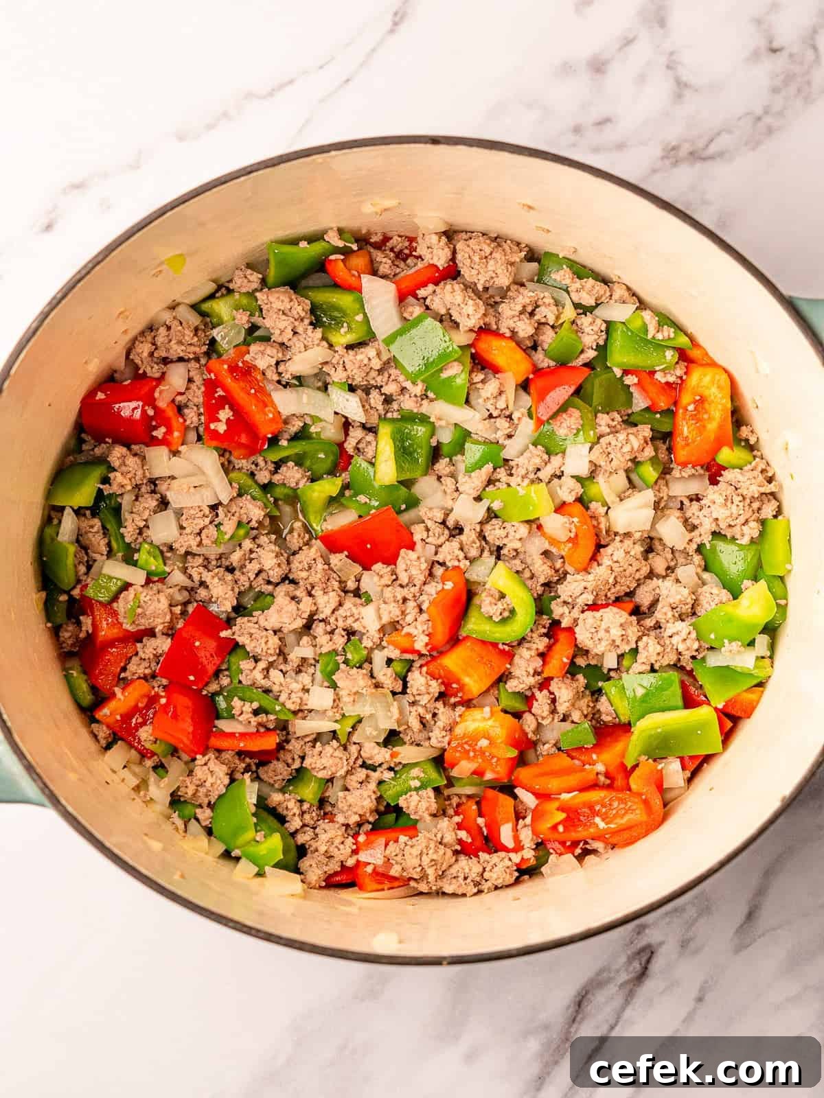 Ground turkey with diced onion and bell peppers in a Dutch oven.