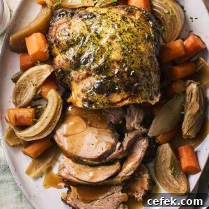 A slow cooker leg of lamb on a plate, ready to serve, with vegetables around the side.