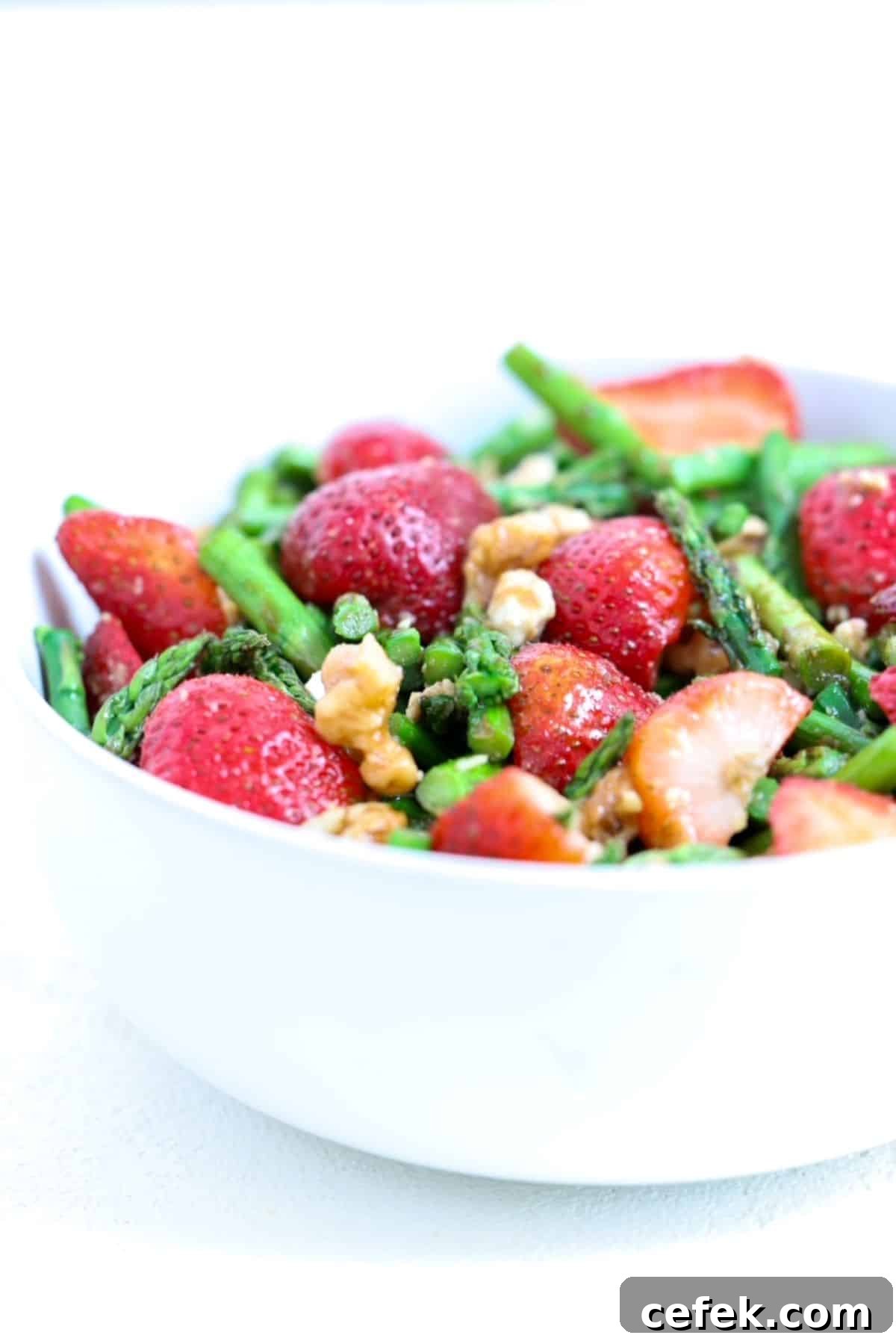 Cold asparagus salad with strawberries in a white serving bowl.