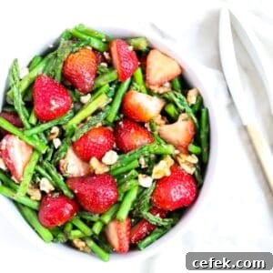 Cold Asparagus Salad with strawberries in a white serving bowl with white and gold tongs next to the bowl.
