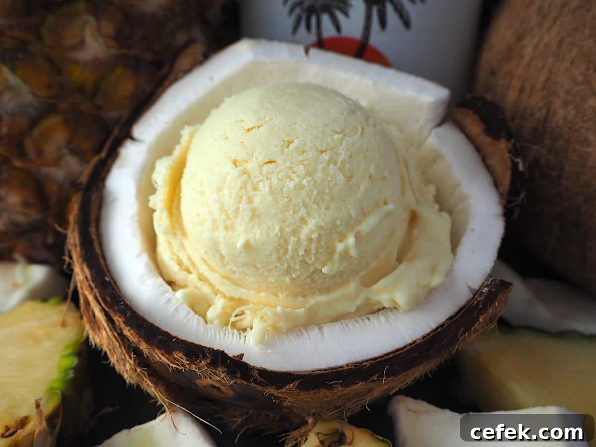 Scoop of pina cola ice cream in half a coconut, with pineapple and coconut rum bottle in background.