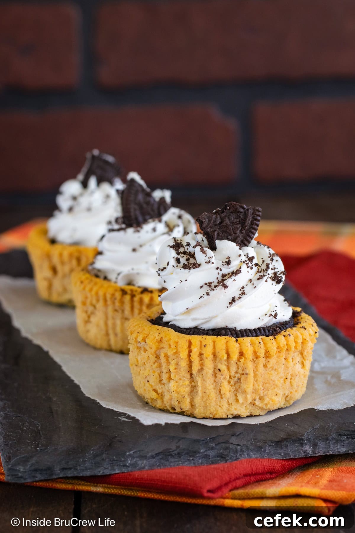 Three pumpkin Oreo cheesecakes topped with whipped cream on a black board.