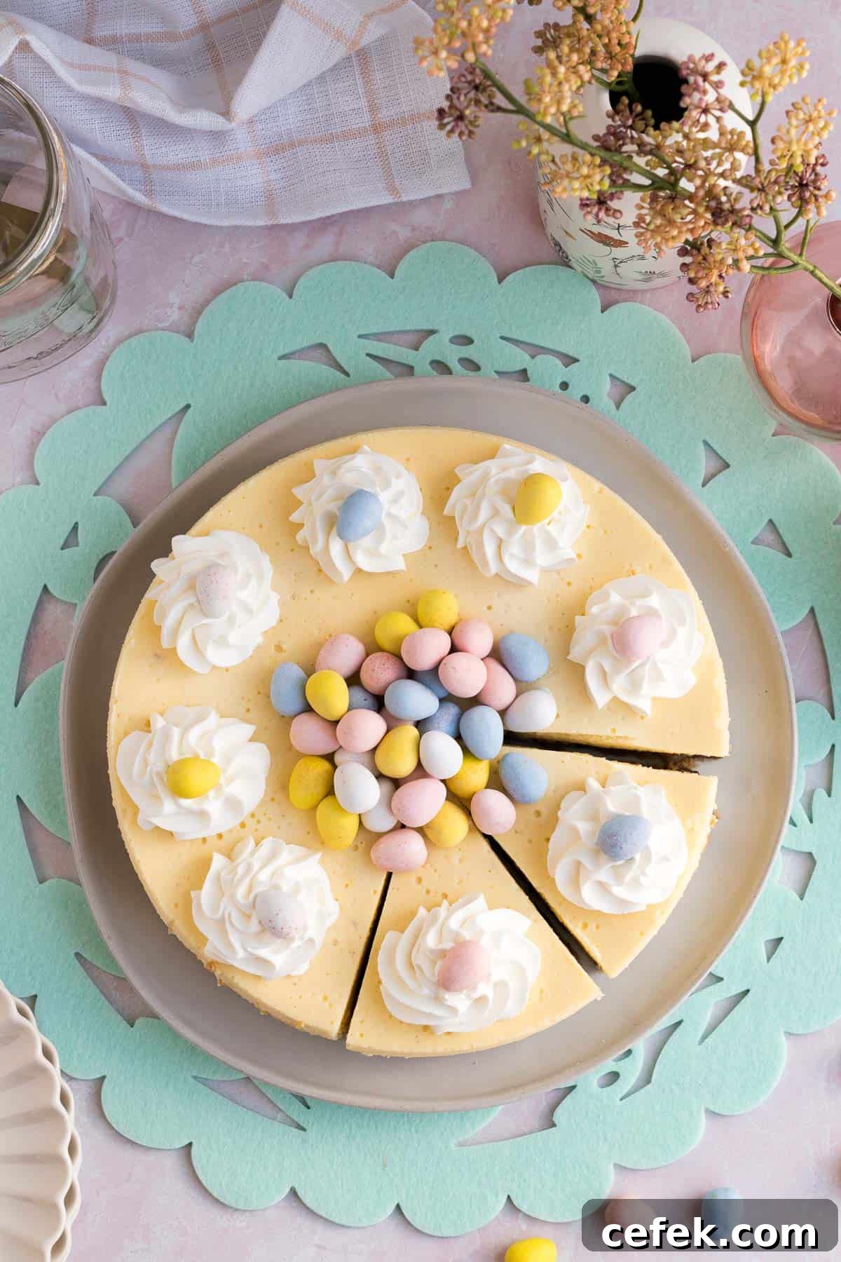 Top view of an Easter egg cheesecake with whipped cream and mini eggs piled on top and 2 slices cut sitting on a green Easter placemat