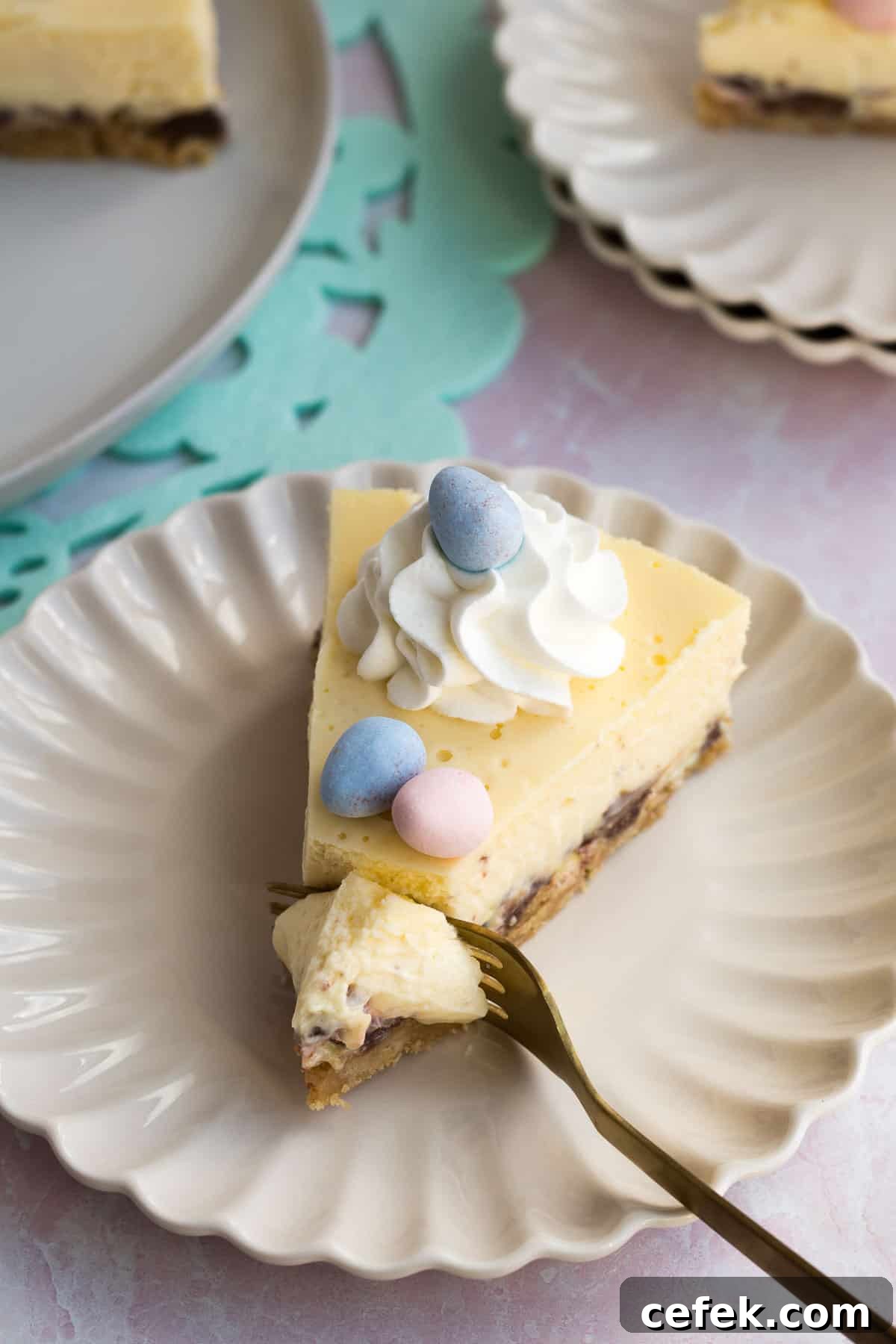 a cream scalloped plate with a slice of easter egg cheesecake with a gold fork cutting into it