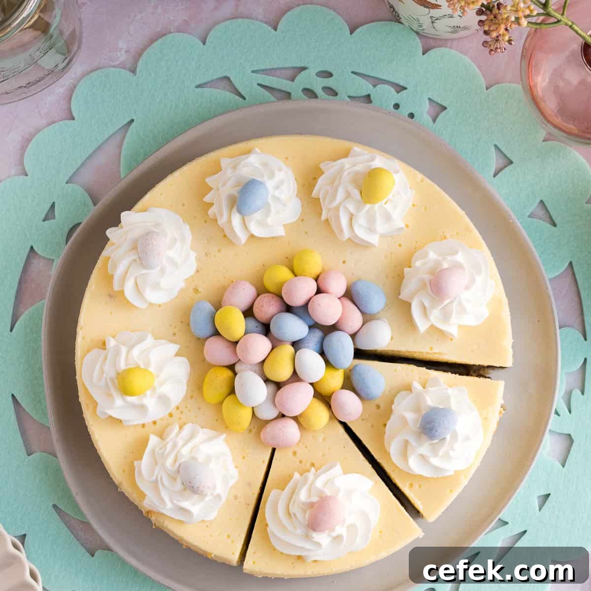 Top view of an Easter egg cheesecake with whipped cream and mini eggs piled on top and 2 slices cut sitting on a green Easter placemat
