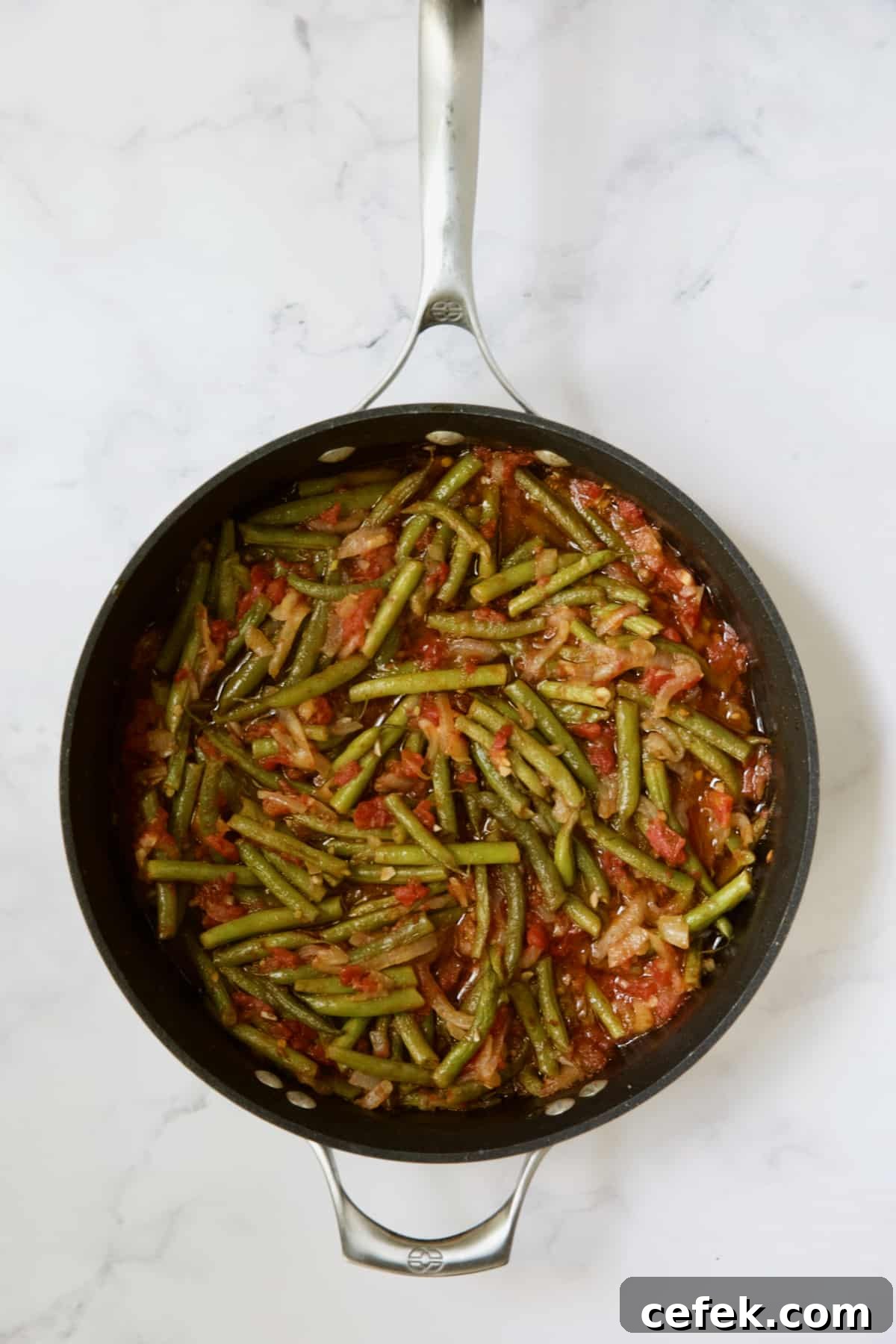 Cooked green beans and tomatoes in skillet.