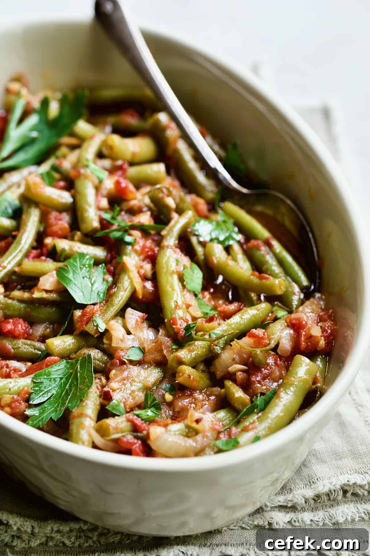 Mediterranean Braised Green Beans with Tomatoes in oval serving dish with serving spoon.