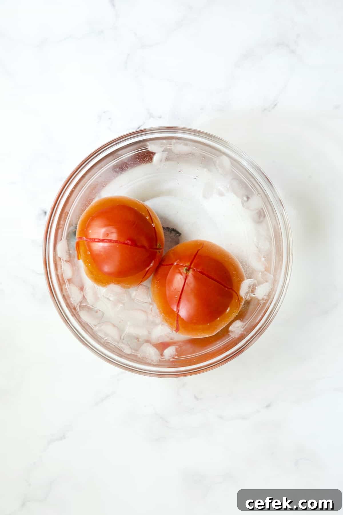 Two tomatoes in ice bath in glass bowl.