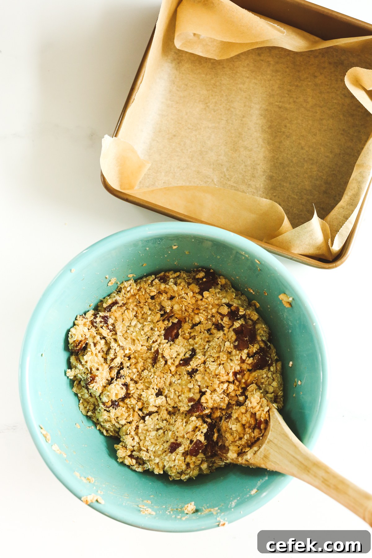 ingredients mixed together in a blue bowl next to a parchment paper lined square pan
