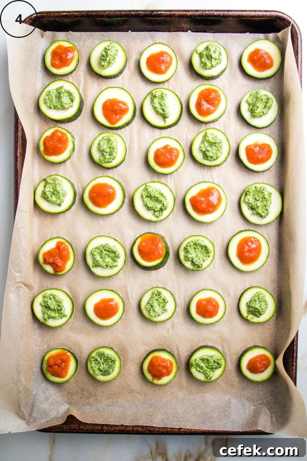 Baking tray with rows of sliced zucchini rounds topped with marinara or pesto.