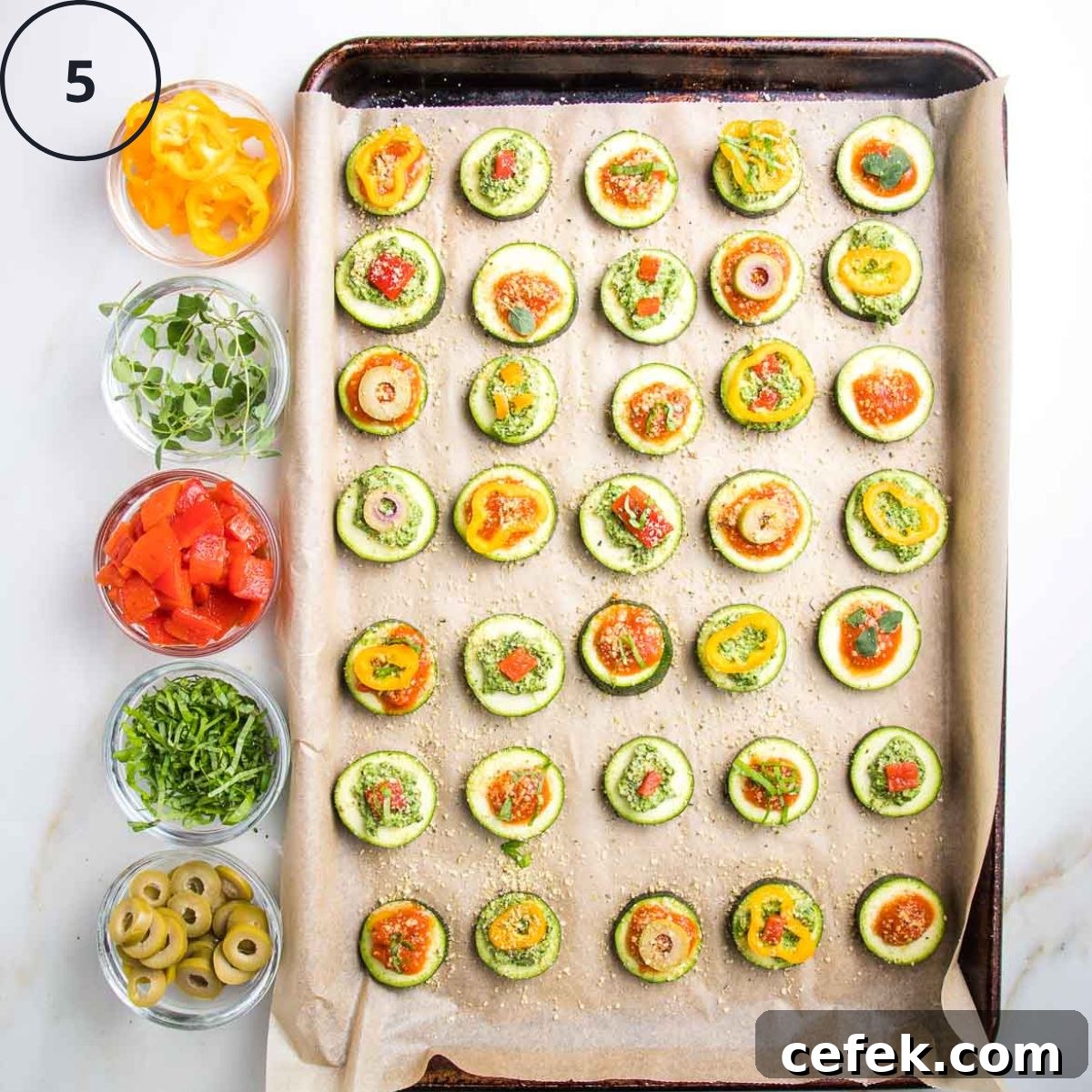 Baking tray of zucchini pizza bites with small dishes on the side with toppings.