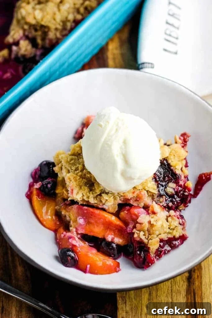 A bowl of blueberry peach crisp with a scoop of vanilla ice cream
