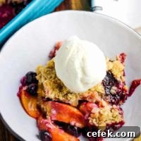 A bowl of blueberry peach crisp with a scoop of vanilla ice cream