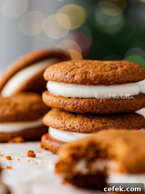 Stacked gingerbread whoopie pies on white parchment paper with holiday tree background.