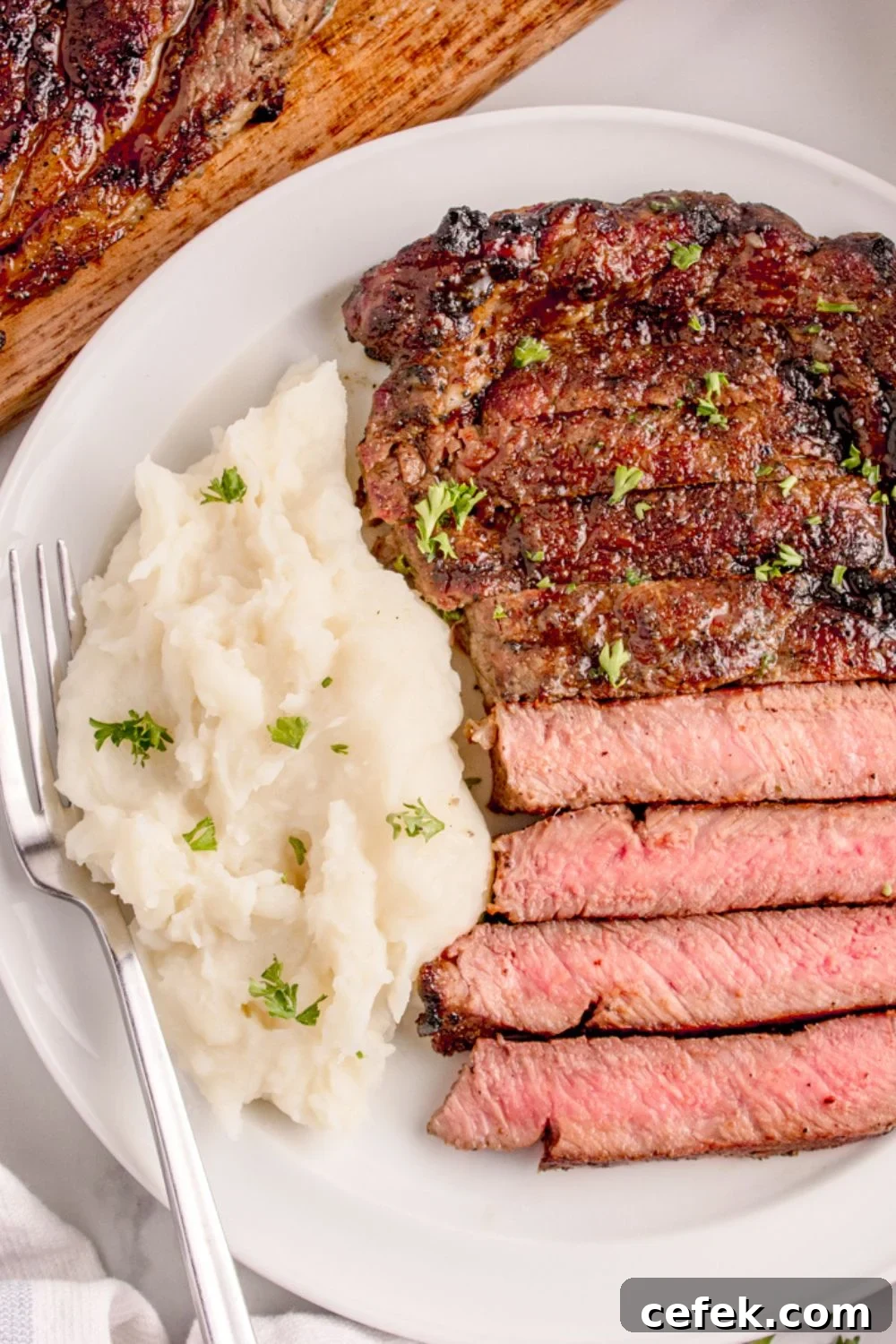 Grilled Ribeye Steak on plate with mashed potatoes to side and a fork on side of plate 