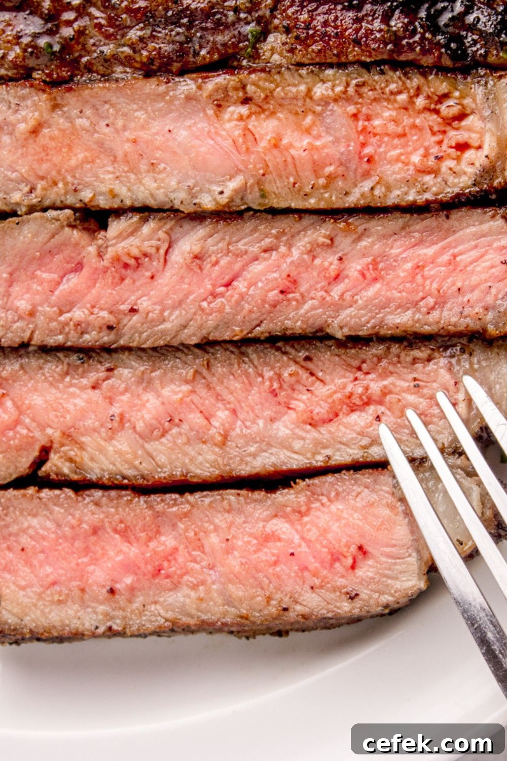 Grilled Ribeye Steak sliced into strips, with a close up of the redness and a fork to side 