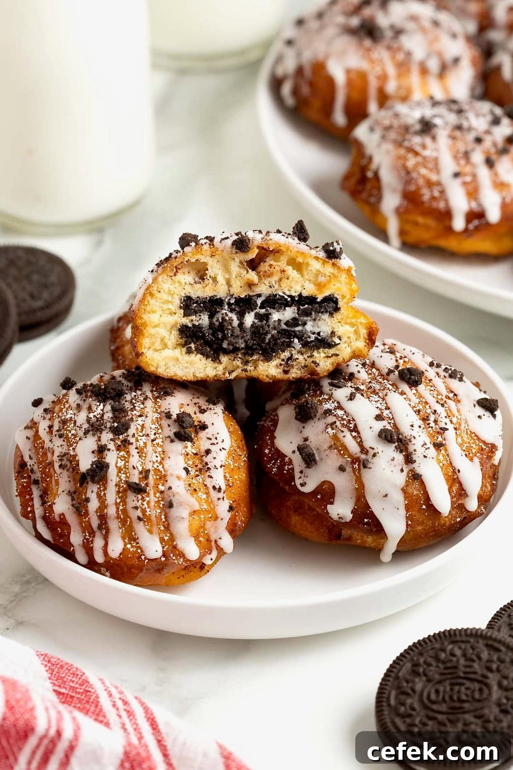 A white rimmed plate holding three fried cinnamon rolls with Oreos in the middle. The one on top is cut open to reveal the Oreo inside.
