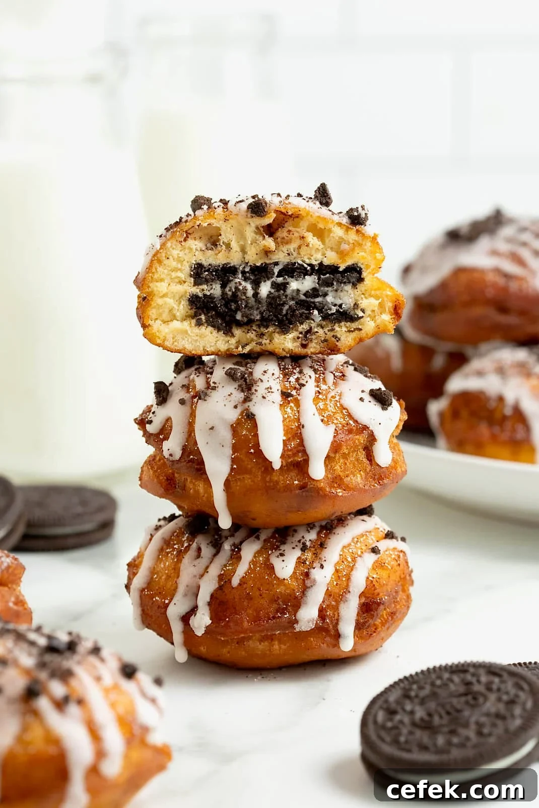 A stack of three cinnamon roll fried Oreos on a white marble counter. The top fried Oreo has a bite out of it revealing the Oreo inside.