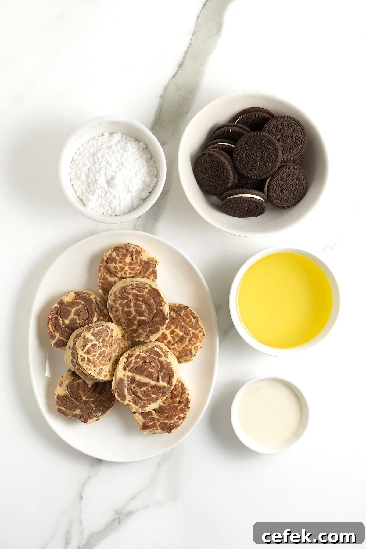 ingredients to make cinnamon roll deep fried Oreos in small white dishes on a white marble counter.