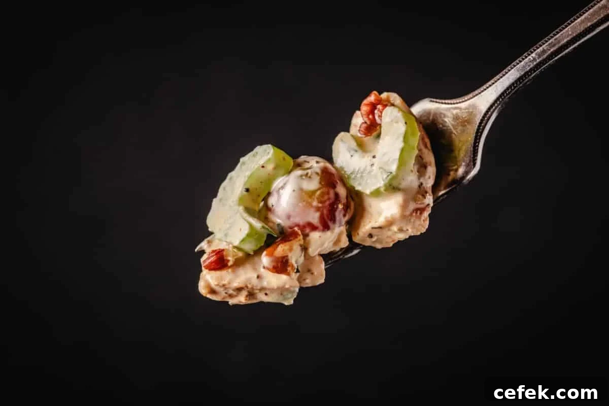 A fork holding chopped chicken, celery, and grapes.