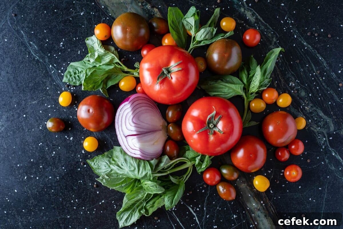 Fresh tomatoes, onions, and leafy greens on a black counter.