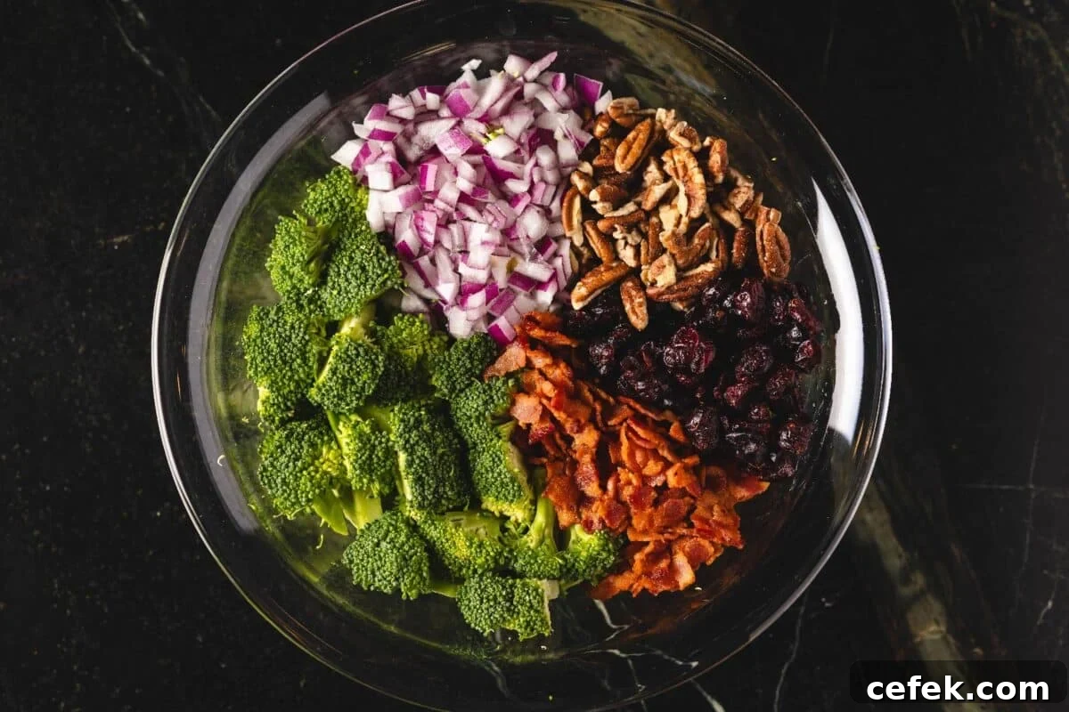 Chopped broccoli, onions, and nuts in a glass bowl.