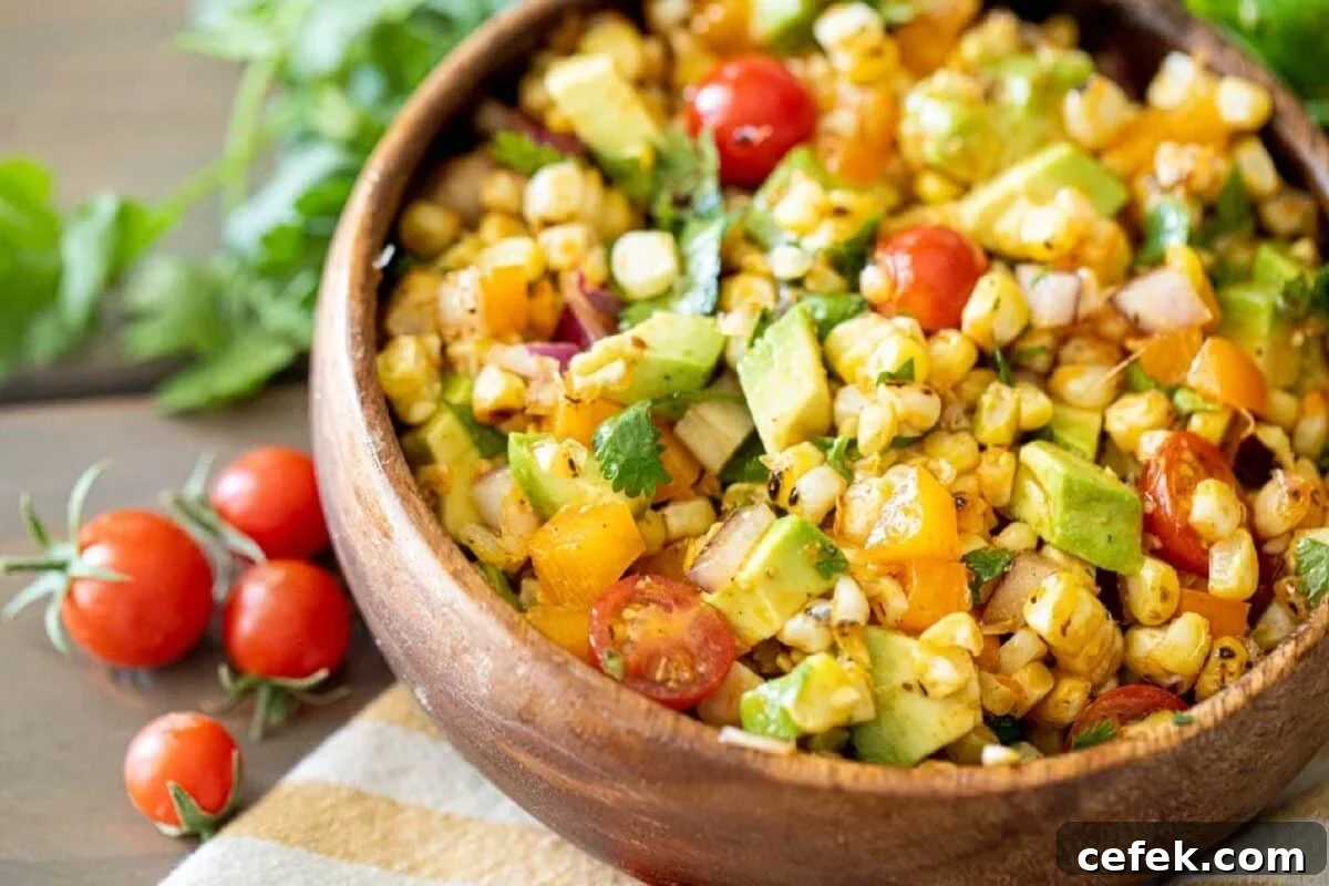 A wooden bowl filled with a recipe for corn salad, next to some cherry tomatoes.