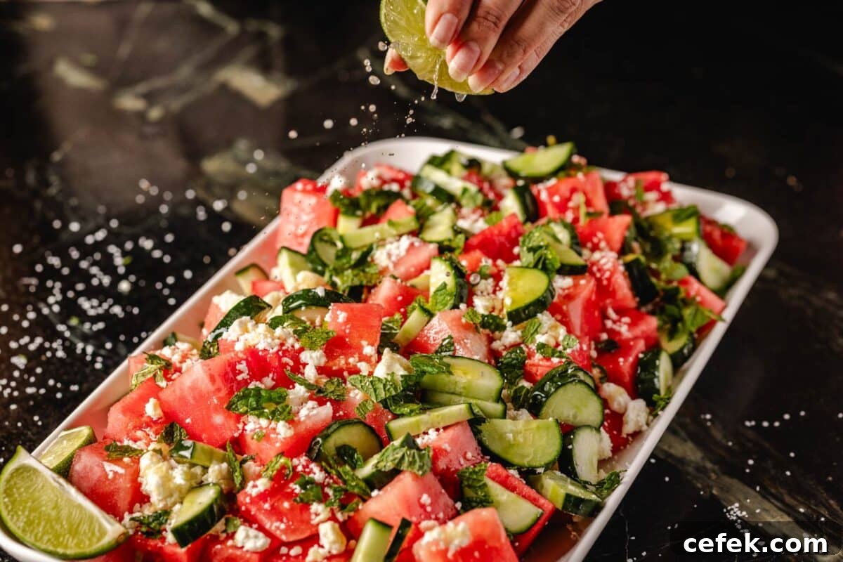 Sliced watermelon and cucumber on a large platter, with a hand squeezing fresh juice from a lime onto them.