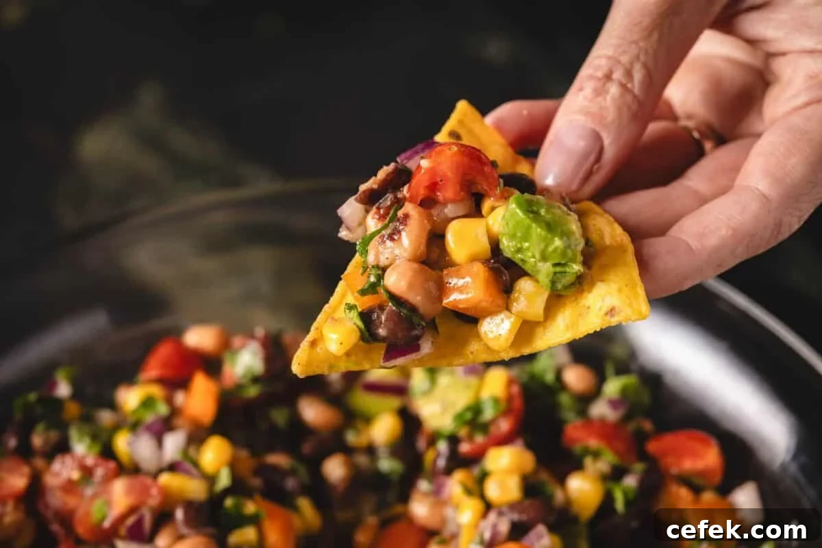 A chip holding salsa above a bowl of more salsa.