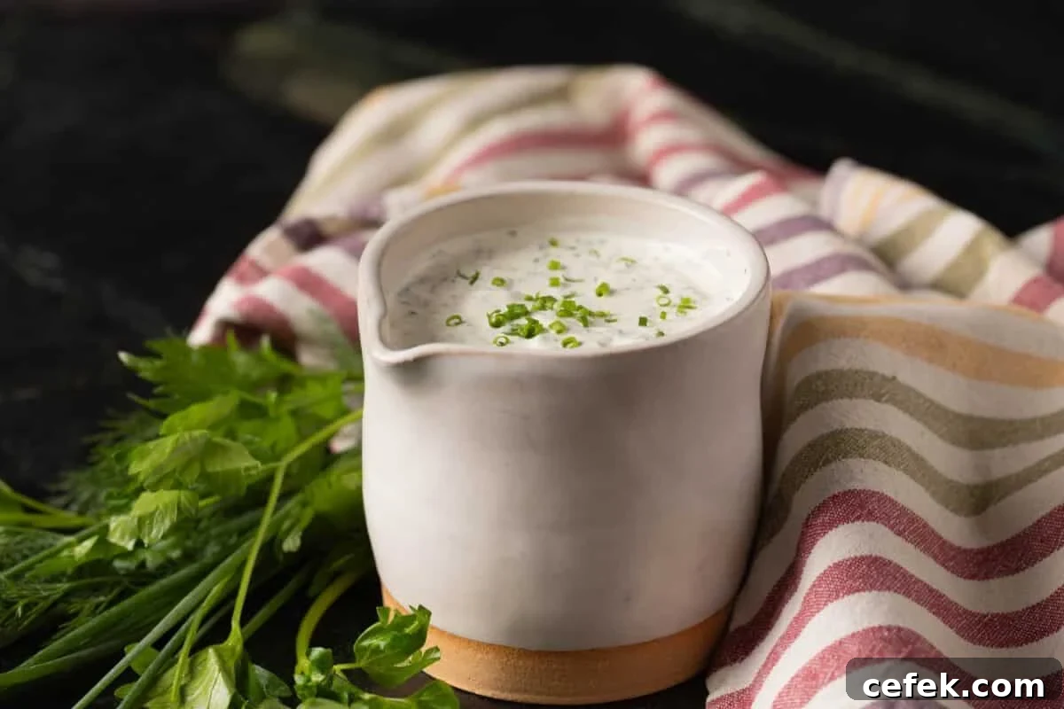 A white jar of ranch dressing next to a tablecloth and fresh herbs.