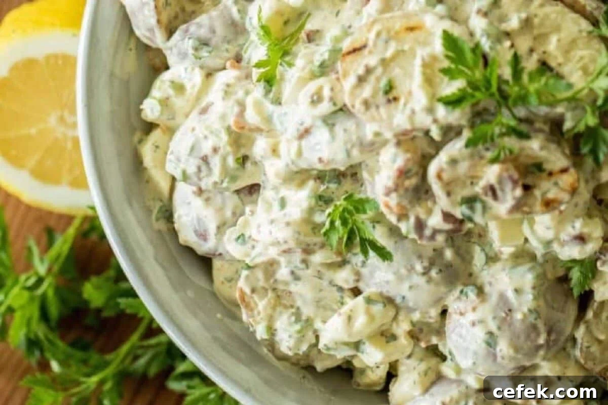 A potato salad recipe in a white bowl next to a lemon wedge and herb garnish.