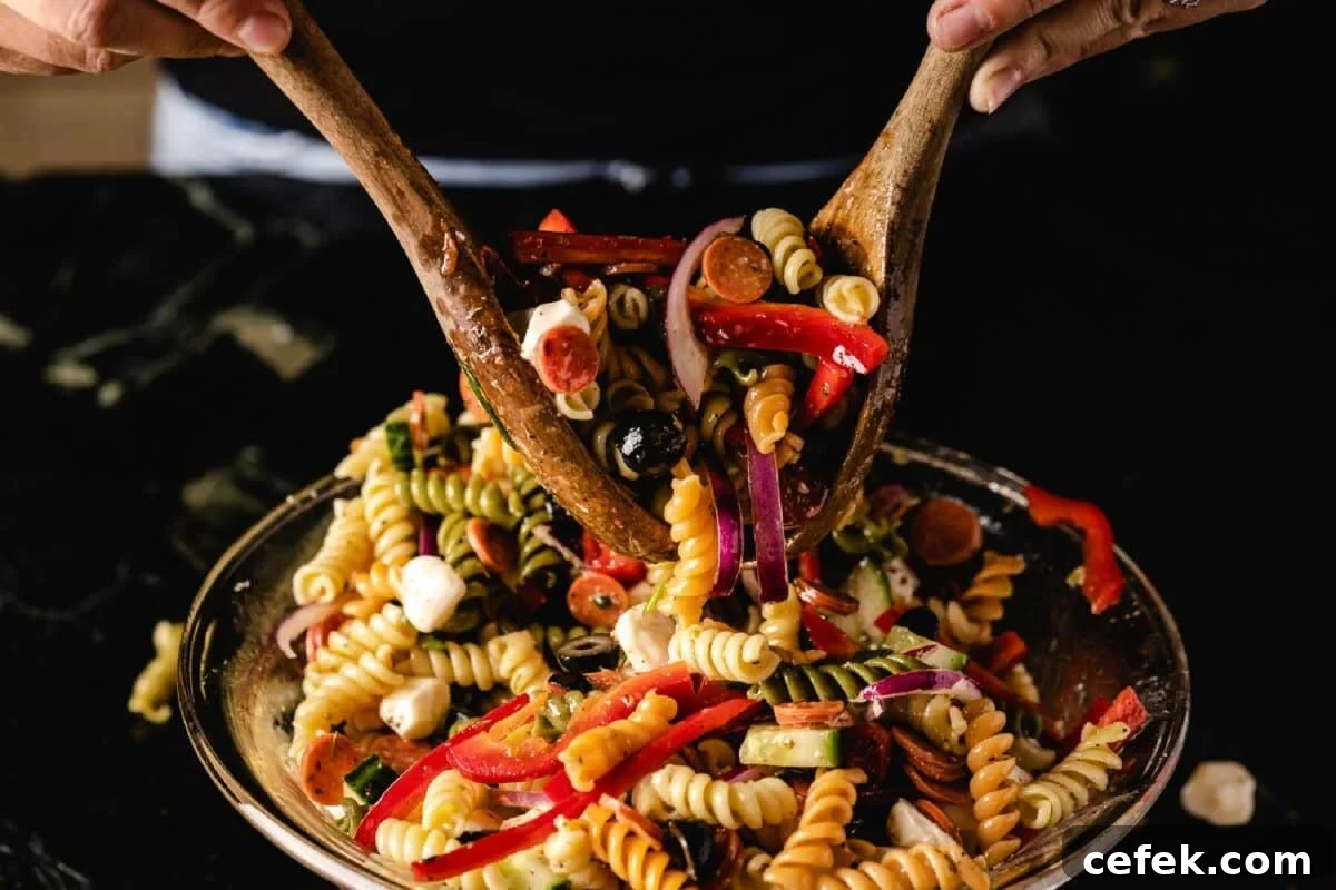 Wooden serving tools tossing a pasta salad in a glass bowl.