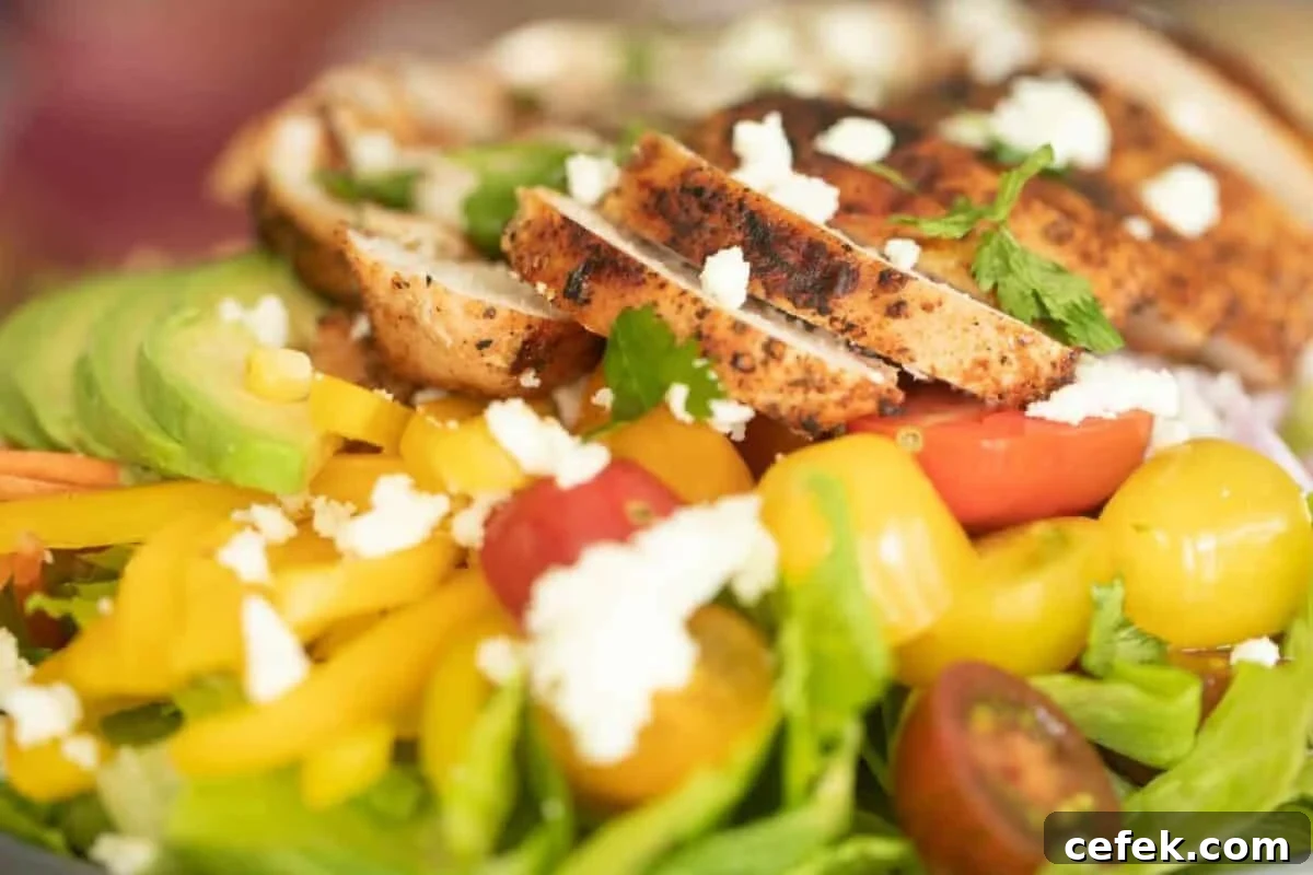 Sliced chicken breast pieces on a bed of lettuce and other sliced veggies.