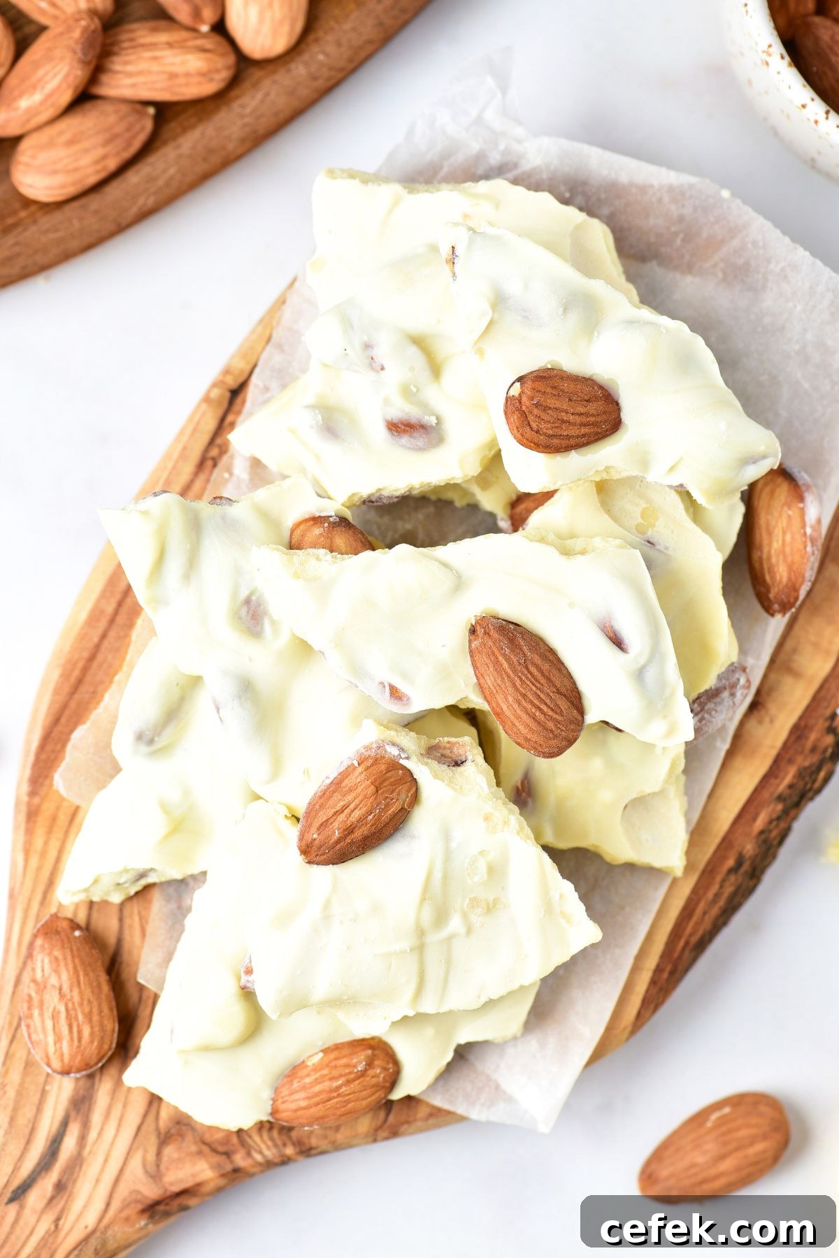 Top down view of white chocolate almond bark on parchment-lined wooden board.