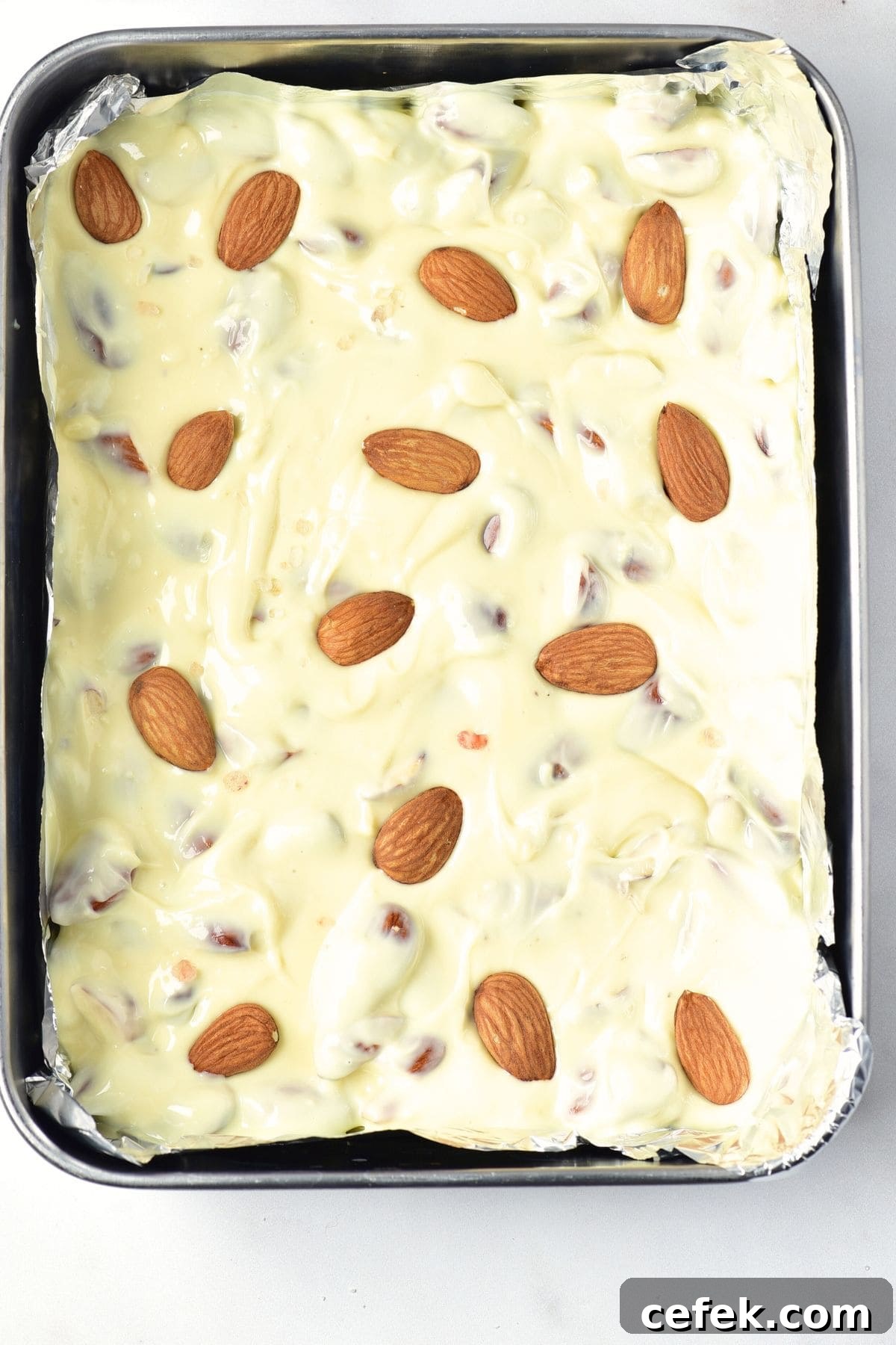 Melted white chocolate topped with whole almonds in baking pan