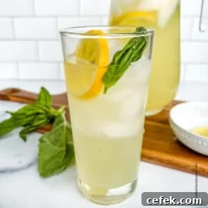 Freshly made basil lemonade served over ice in a tall drinking glass, garnished with basil leaves and a lemon slice.